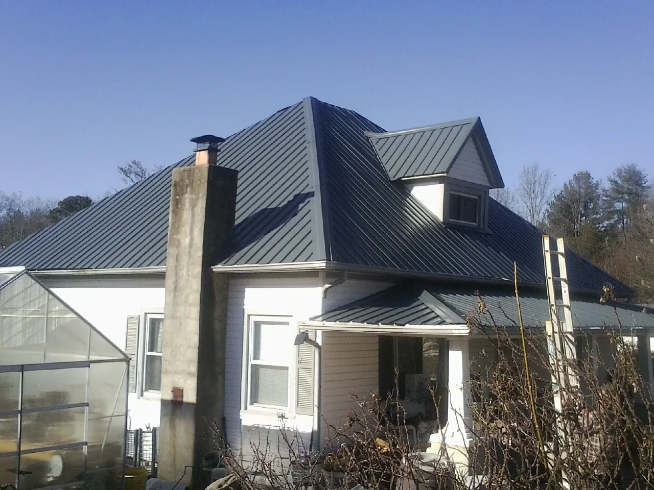 Dark blue standing seam metal roof on a white farmhouse with dormer — Slate & Tile Roof Repair by Roofing Brothers in Saint Petersburg