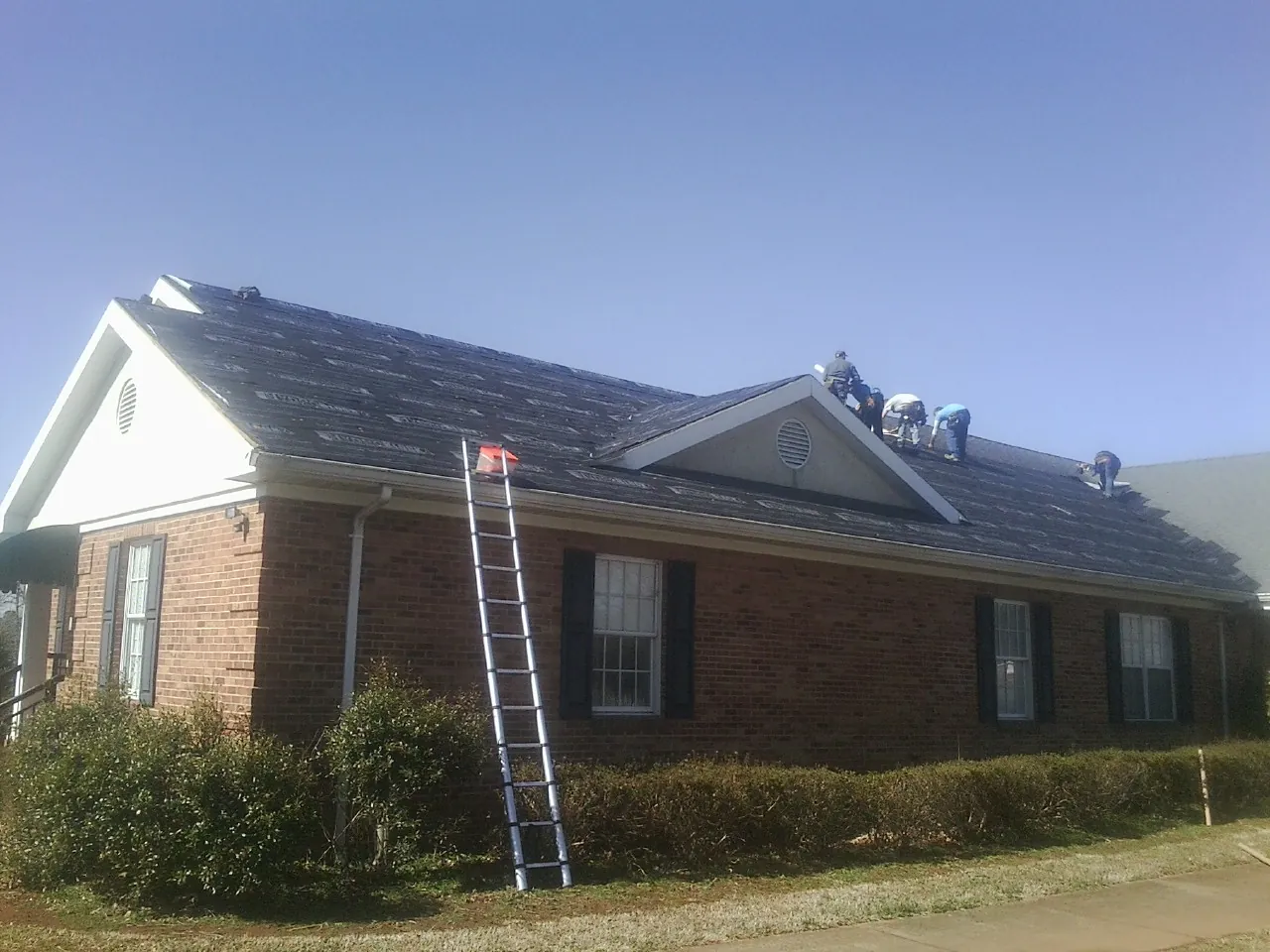 Crew tearing shingles off a brick ranch roof with a ladder set — Metal Roof Repair work by our crew in Saint Petersburg