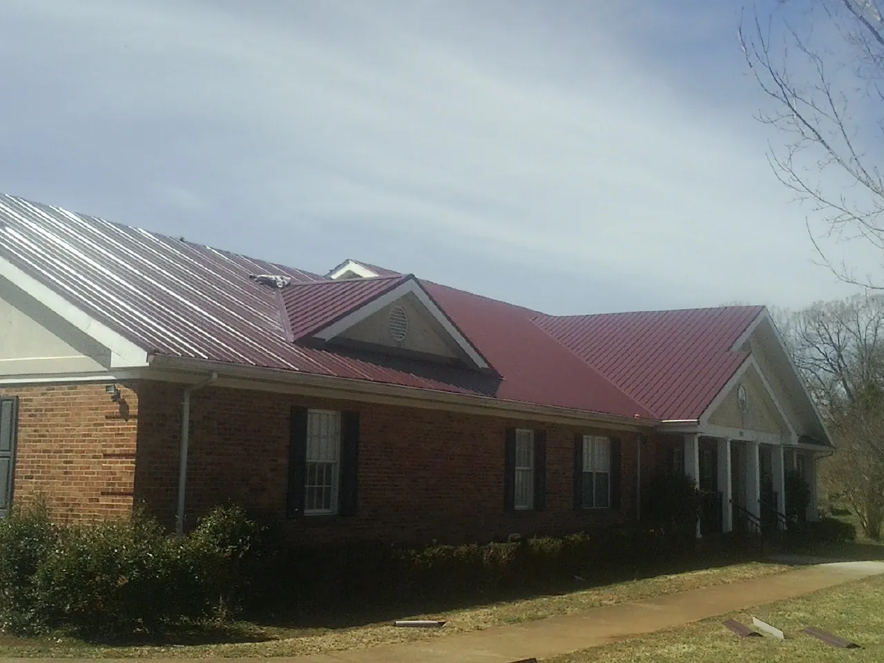 Red metal roof with gabled entries on a long brick building, from a Hail Damage Roof Repair job in Saint Petersburg