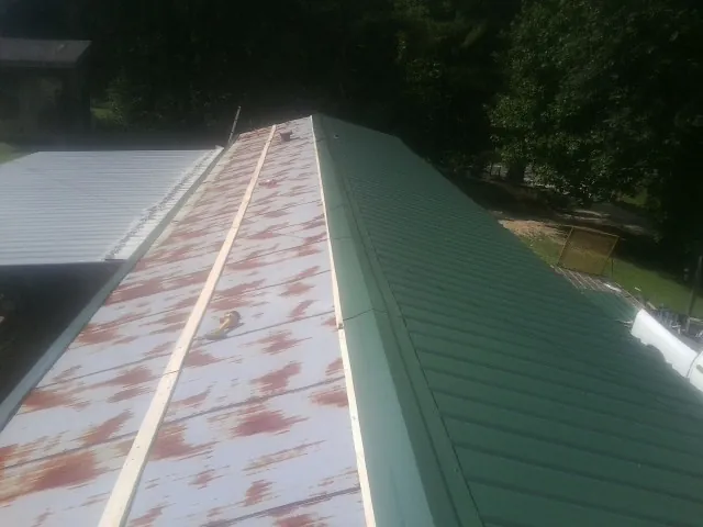 Old rusted panels beside newly installed green metal roofing — Wind Damage Roof Repair by Roofing Brothers in Saint Petersburg