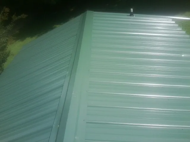 New green metal panels meeting at the ridge of a roof — Flat Roof Repair work by our crew in Saint Petersburg