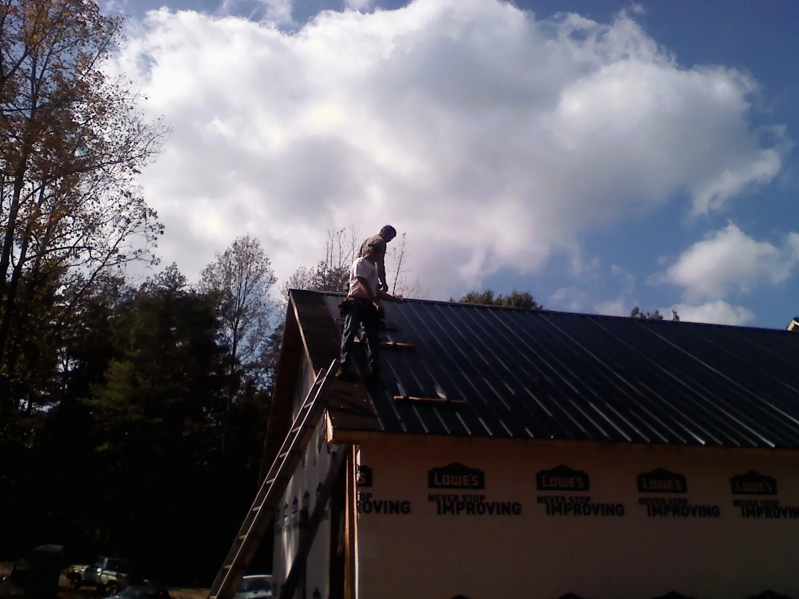 Roofer fastening dark metal panels high against a cloudy sky, from a Roof Inspection job in Saint Petersburg