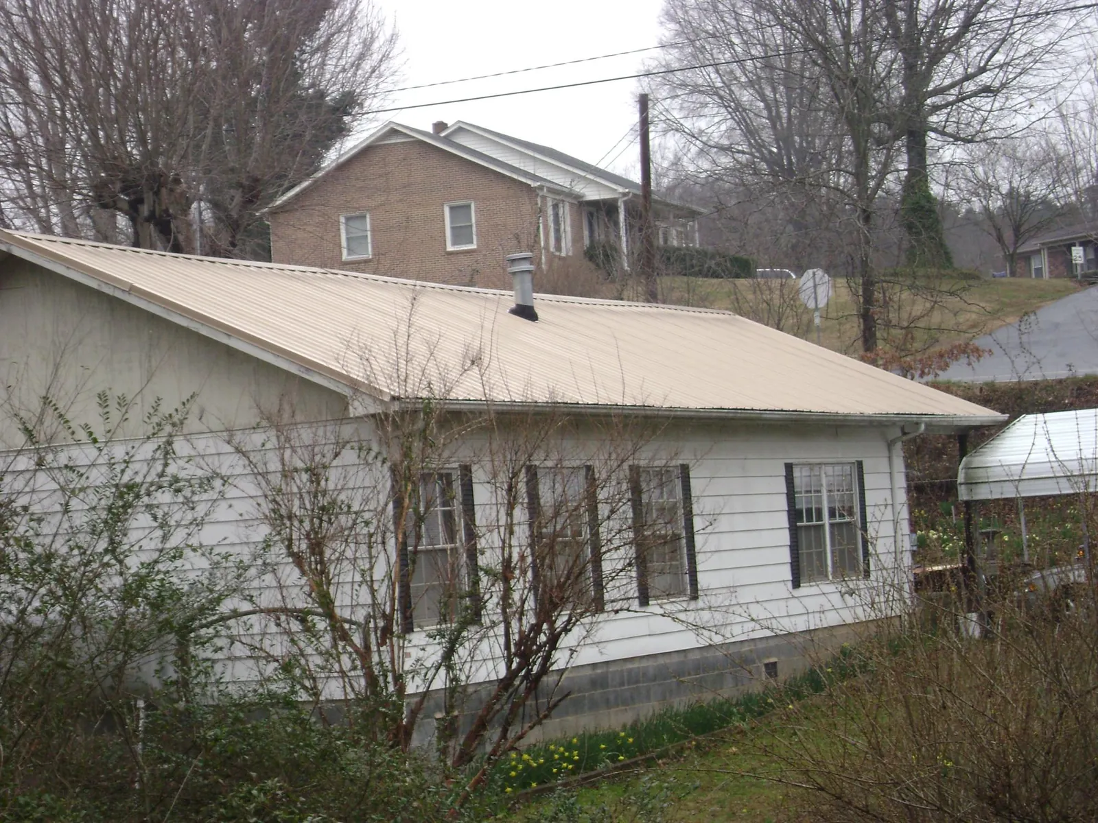Tan metal roof on a white sided house set into a hillside — Commercial Roofing by Roofing Brothers in Saint Petersburg