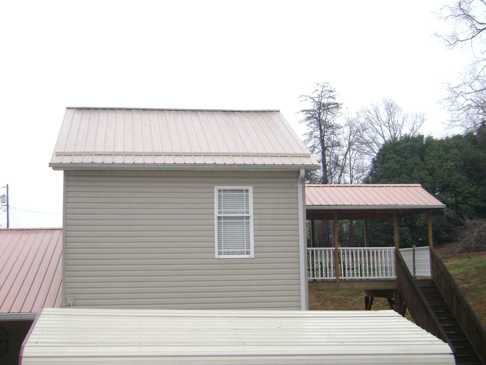 Tan metal roofs on a two story addition and attached porch, from a Roof Replacement job in Saint Petersburg